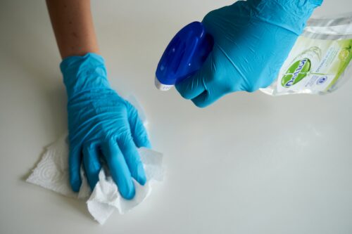 someone cleaning with blue gloves on their hands holding a bottle and a wet wipe