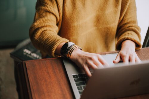 high angle looking down at someone in a yellow jumper working on a laptop from home