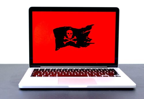 mid view shot of a laptop on a table with a red background and black pirate flag on the screen