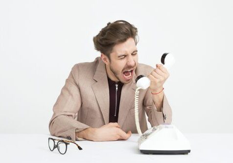 Man angrily yelling into an old-fashioned white landline phone